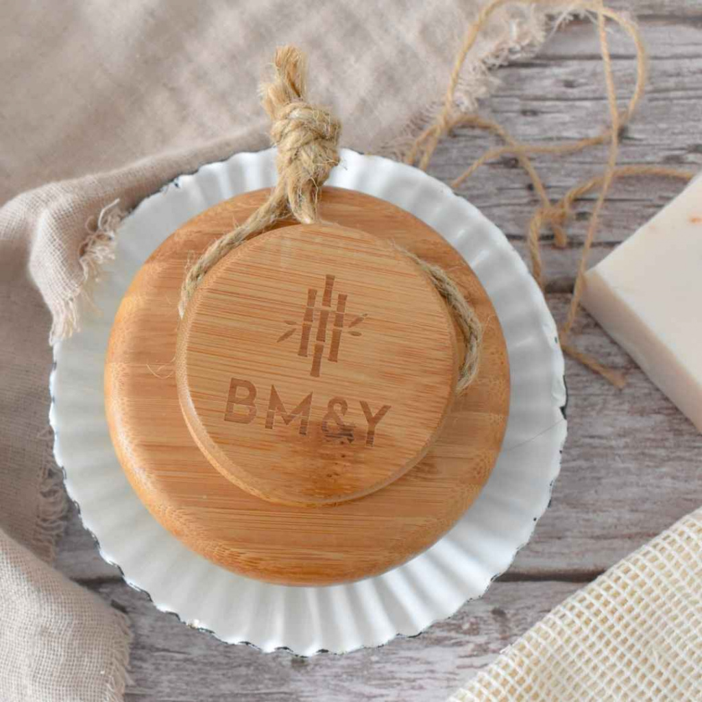 bamboo body brush on white saucer placed on a grey wooden table with a white soap bar to the right hand side