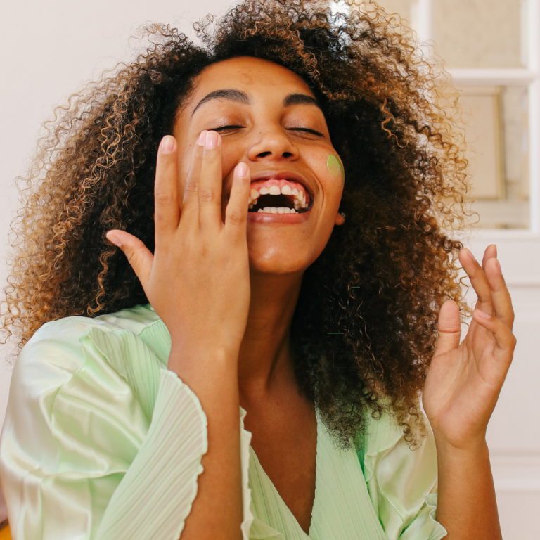 Mixed race woman wearing light green cotton summer robe applying green face cream to cheeks